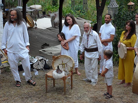 Auf einem Stuhl liegt die Rahmentrommel von Istvan Sky, umgeben von nahestehenden Menschen in weißen Gewändern beim Abschied von István im Hof seines Hauses in Szentbékkállá am 04.08.2024.