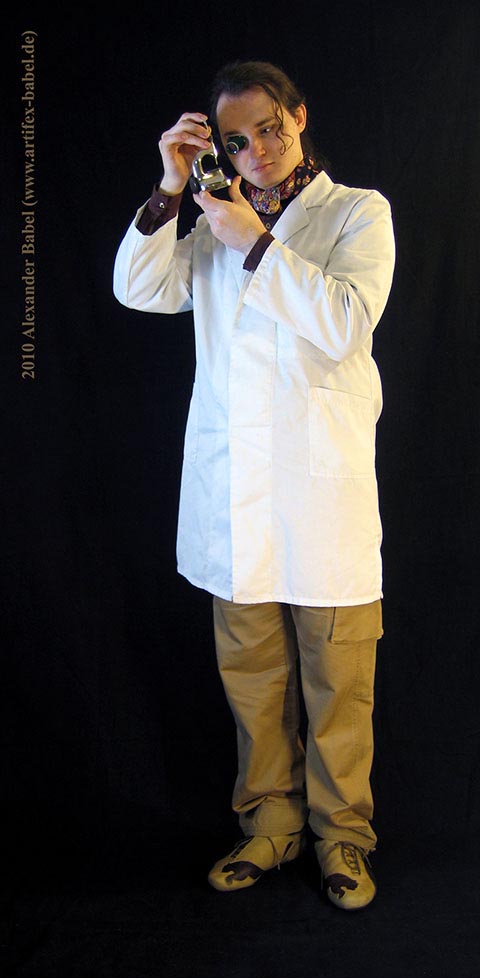 Александр Бабель крупным планом в полный рост, разглядывающий деталь в потансе с лупой.