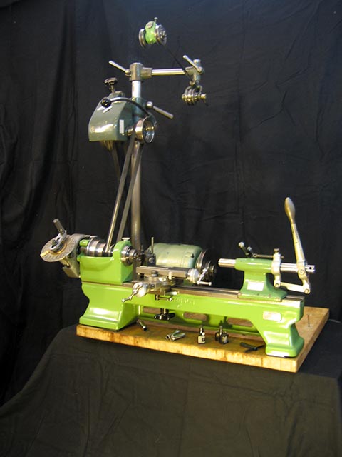 Schaublin 70 lathe with mounted accessories, featuring an overhead drive spindle and belt tensioner. General view.